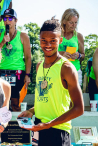 Jakiya smiling after winning second place in the race, holding his prizes and wearing a medal.